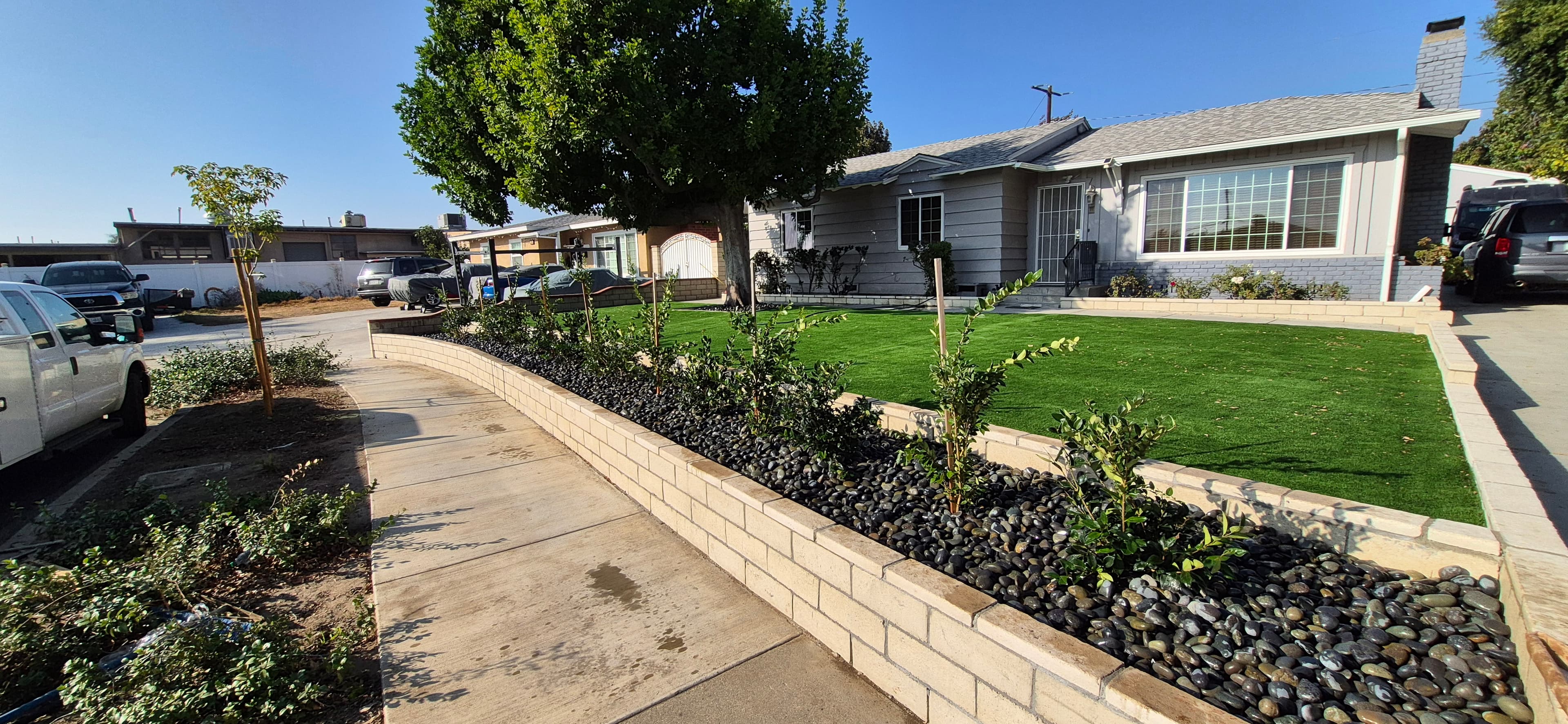 Suburban home with artificial turf and a stone-filled garden bed bordering a concrete sidewalk.