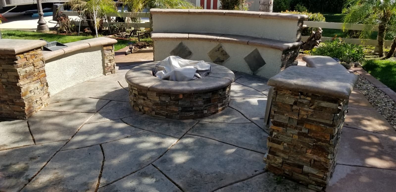 Circular stone fire pit with a cover on a flagstone patio with curved stone seating.