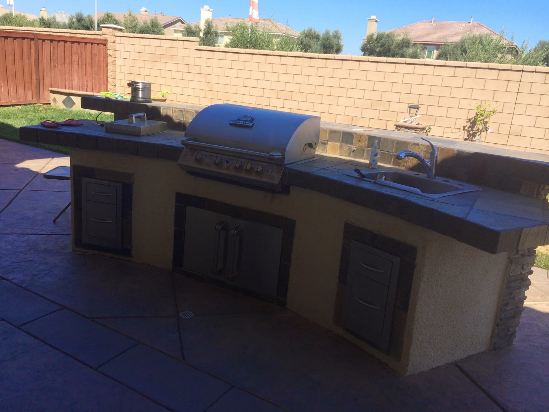 Built-in outdoor kitchen with a stainless steel grill, sink, and storage drawers on a patio.