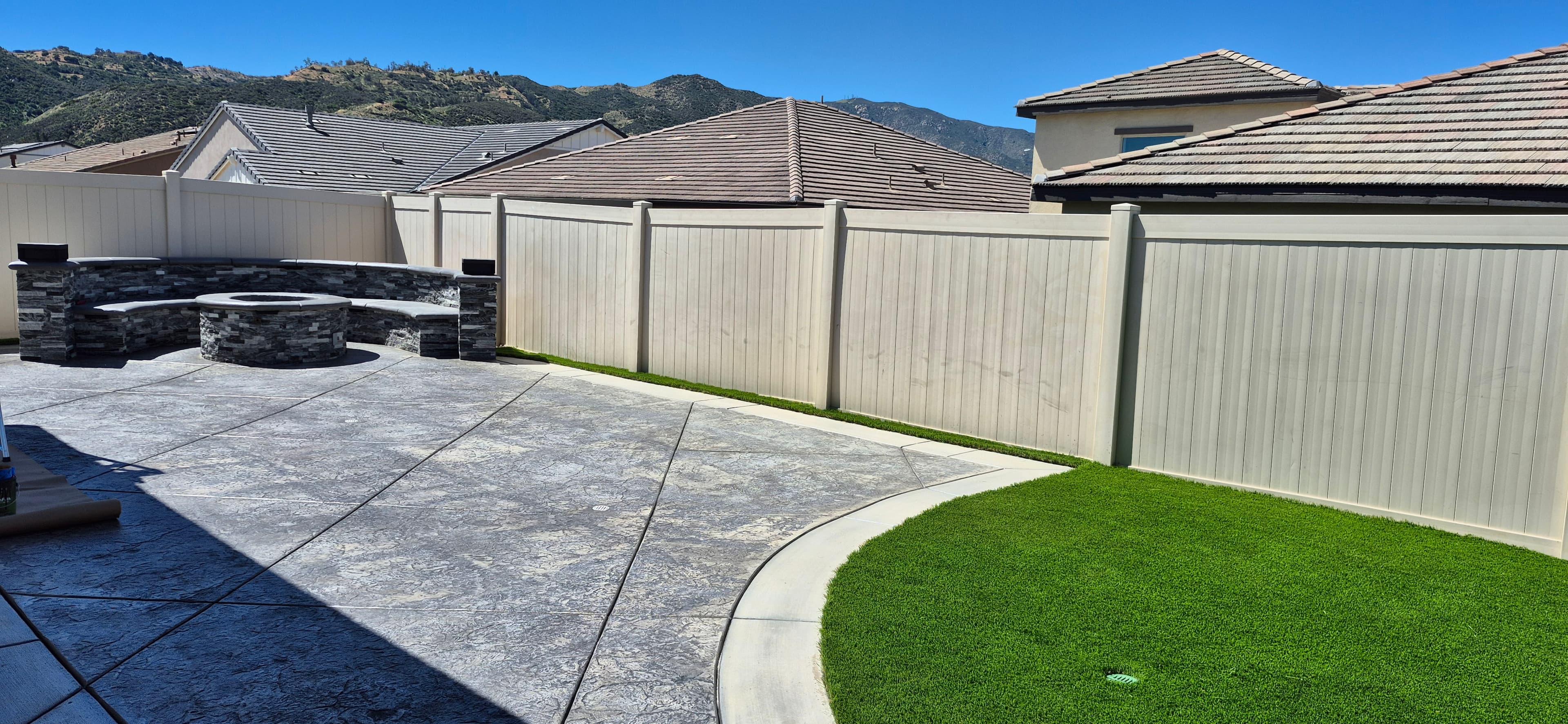 Modern backyard featuring stone fire pit, stamped concrete patio, artificial turf, and mountain views.