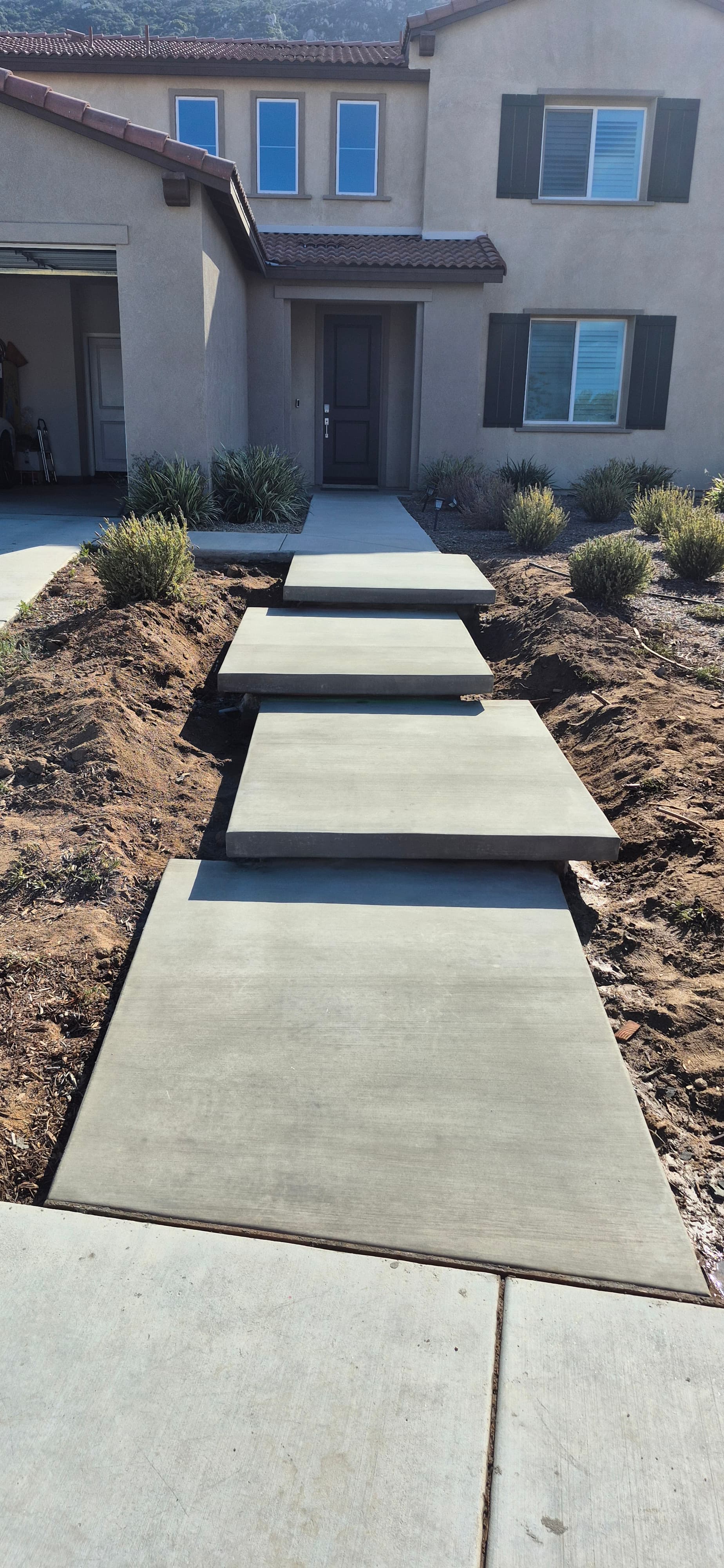 Large rectangular concrete slabs form a floating walkway leading to a modern two-story stucco house.