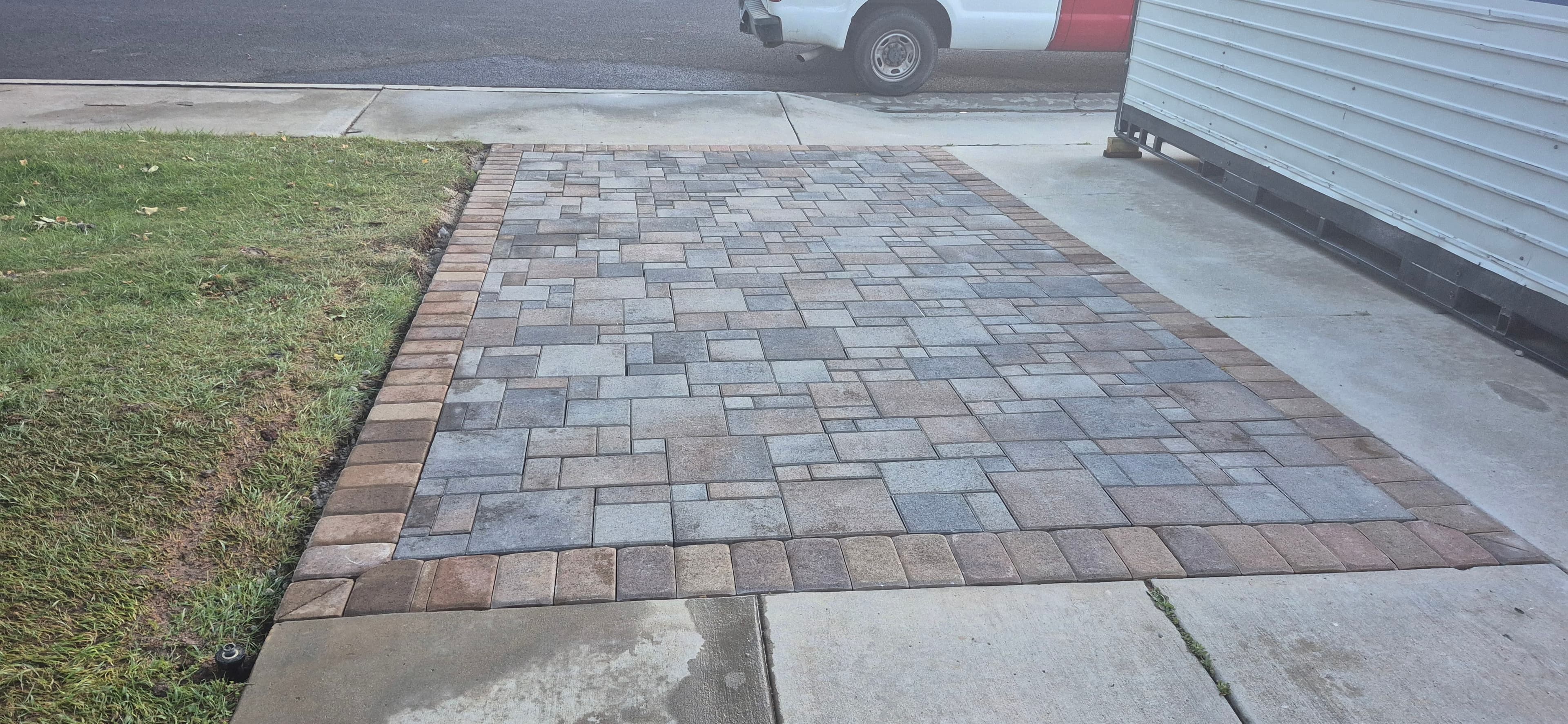 Interlocking grey and brown stone pavers form a rectangular patio bordered by brown bricks.