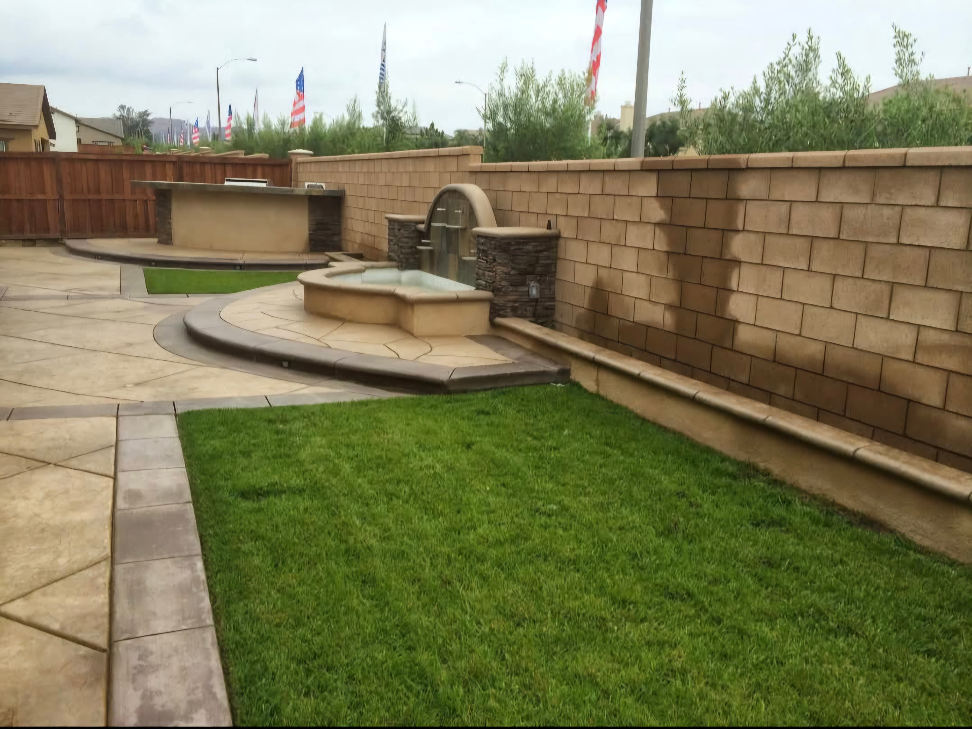 Landscaped backyard with a stone wall water feature, outdoor bar, and green grass lawn.