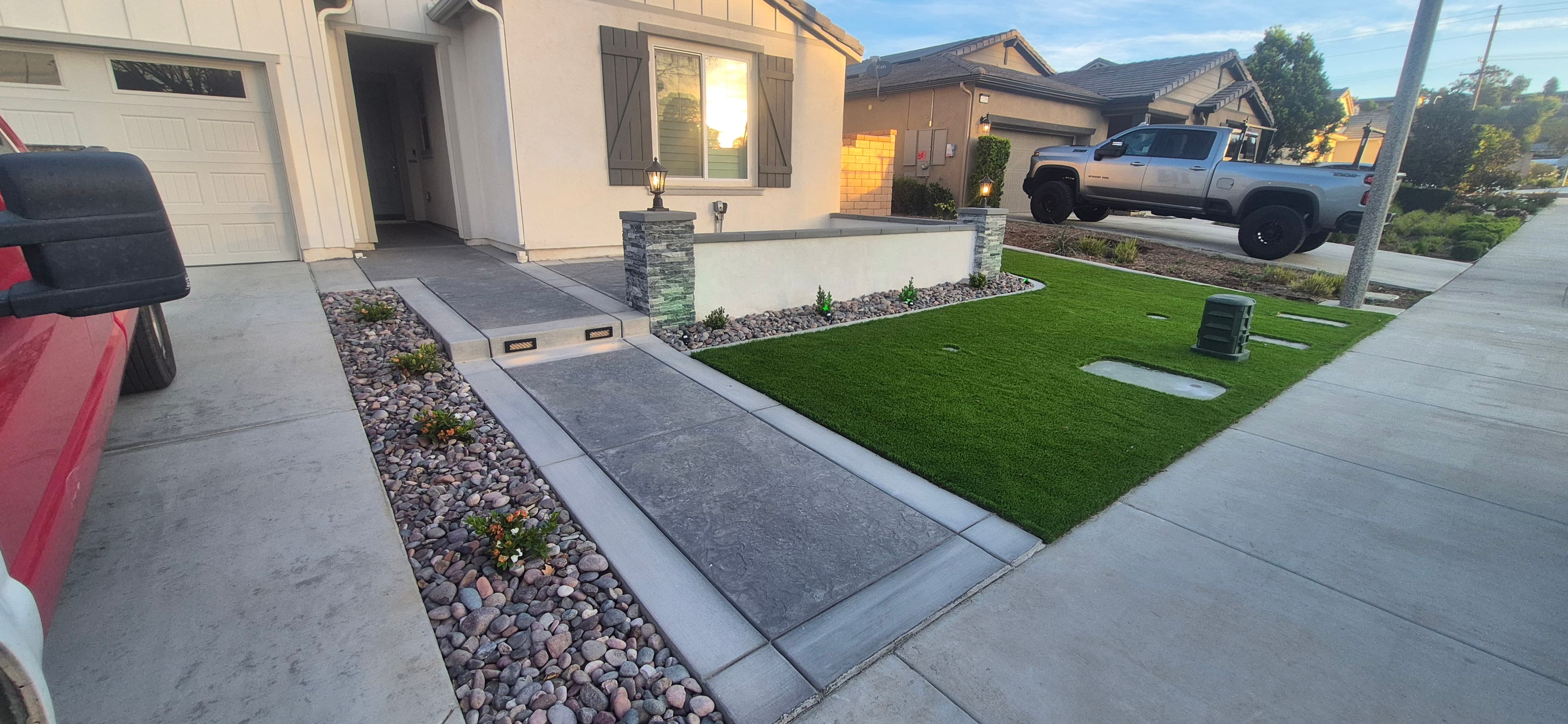Modern front yard with a stamped concrete walkway, artificial turf, and river rock landscaping.