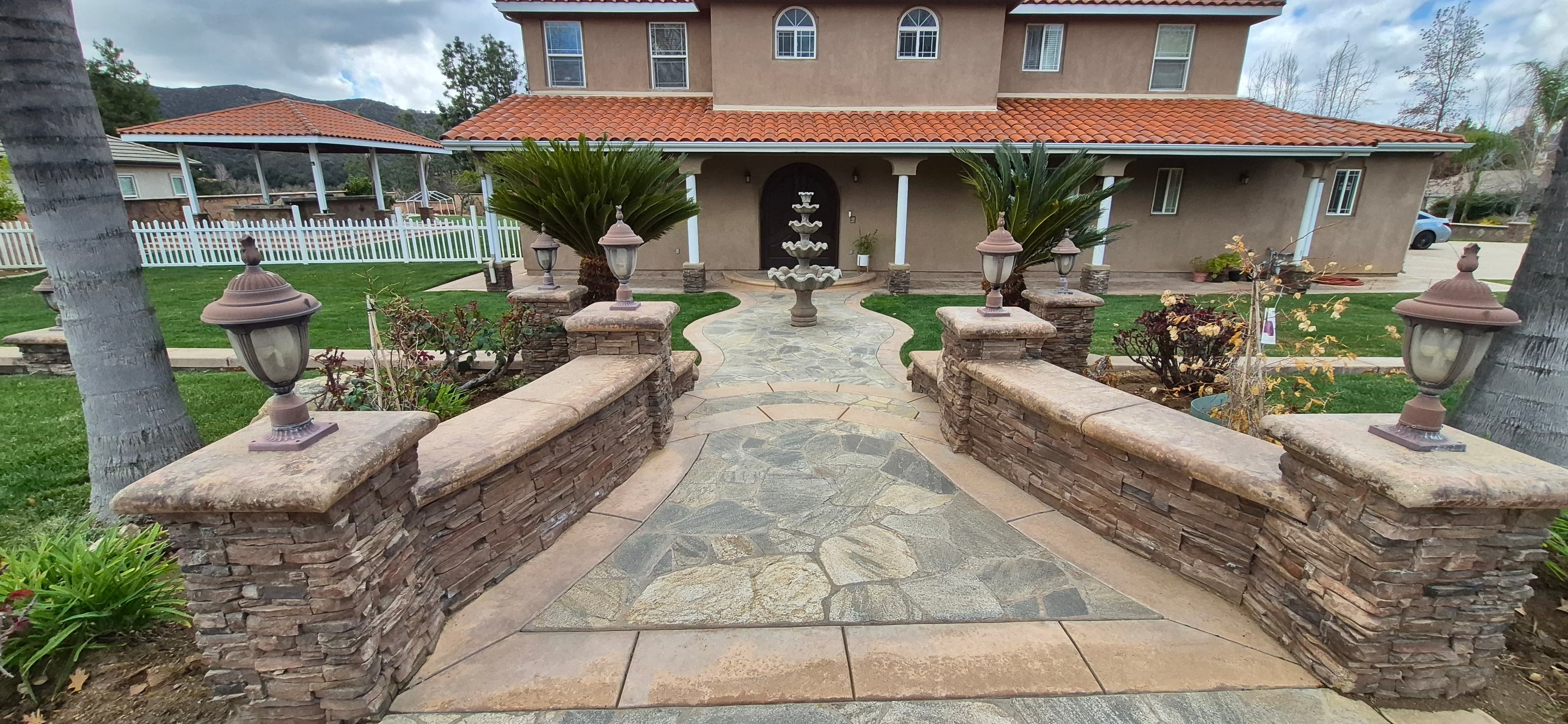 Stone walkway with lanterns and a fountain leading to a house with red tile roof.