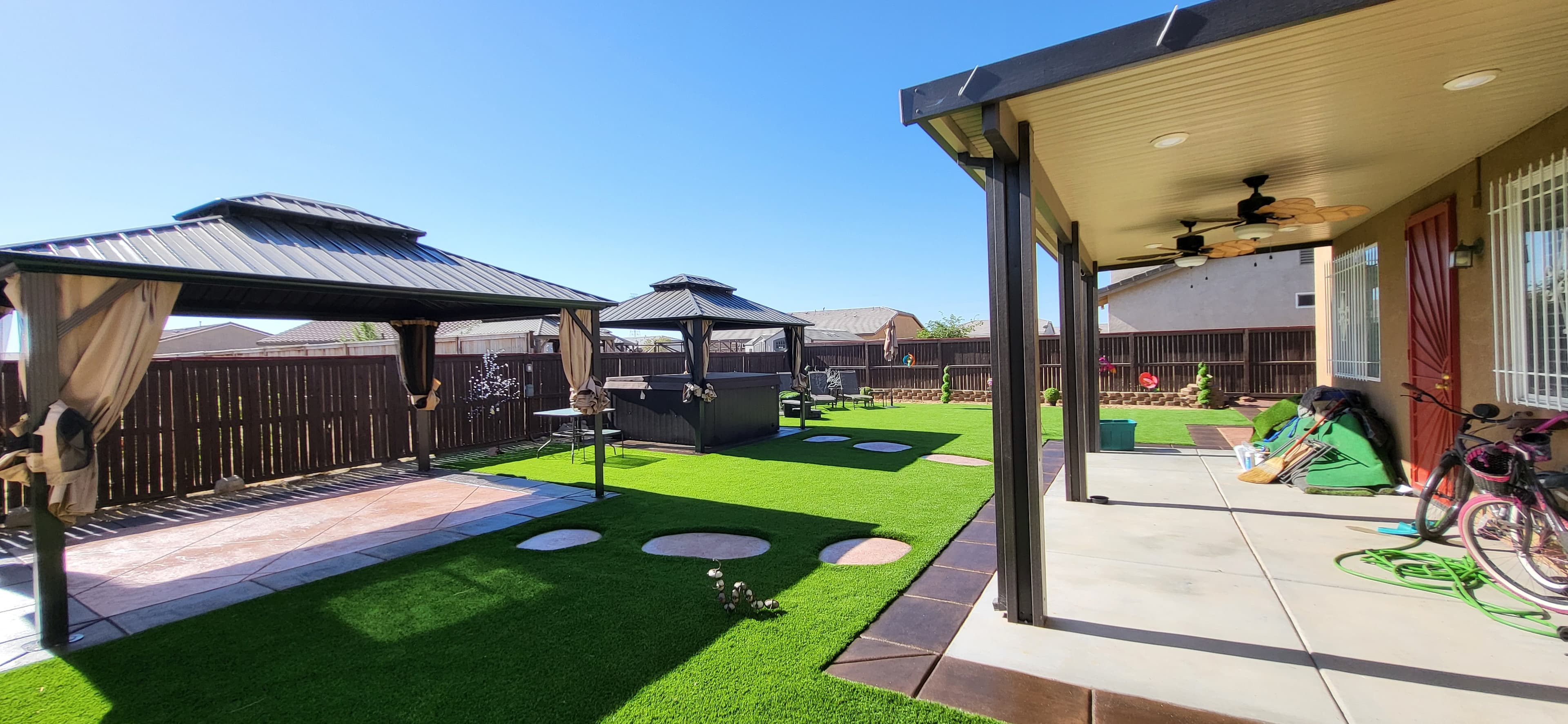Backyard featuring artificial turf, two gazebos, stepping stones, and a covered patio with ceiling fans.