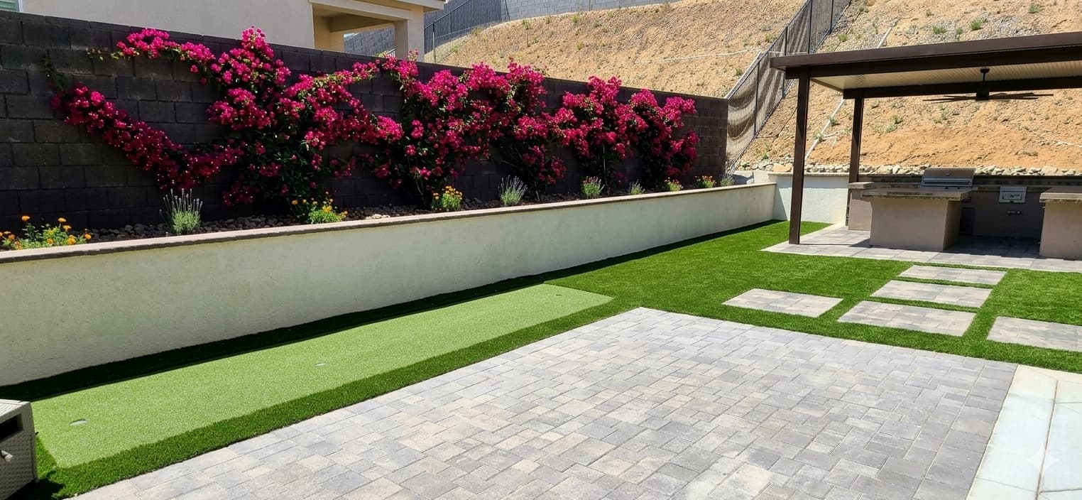 Modern backyard with vibrant pink bougainvillea, artificial turf, stone pavers, and an outdoor kitchen.