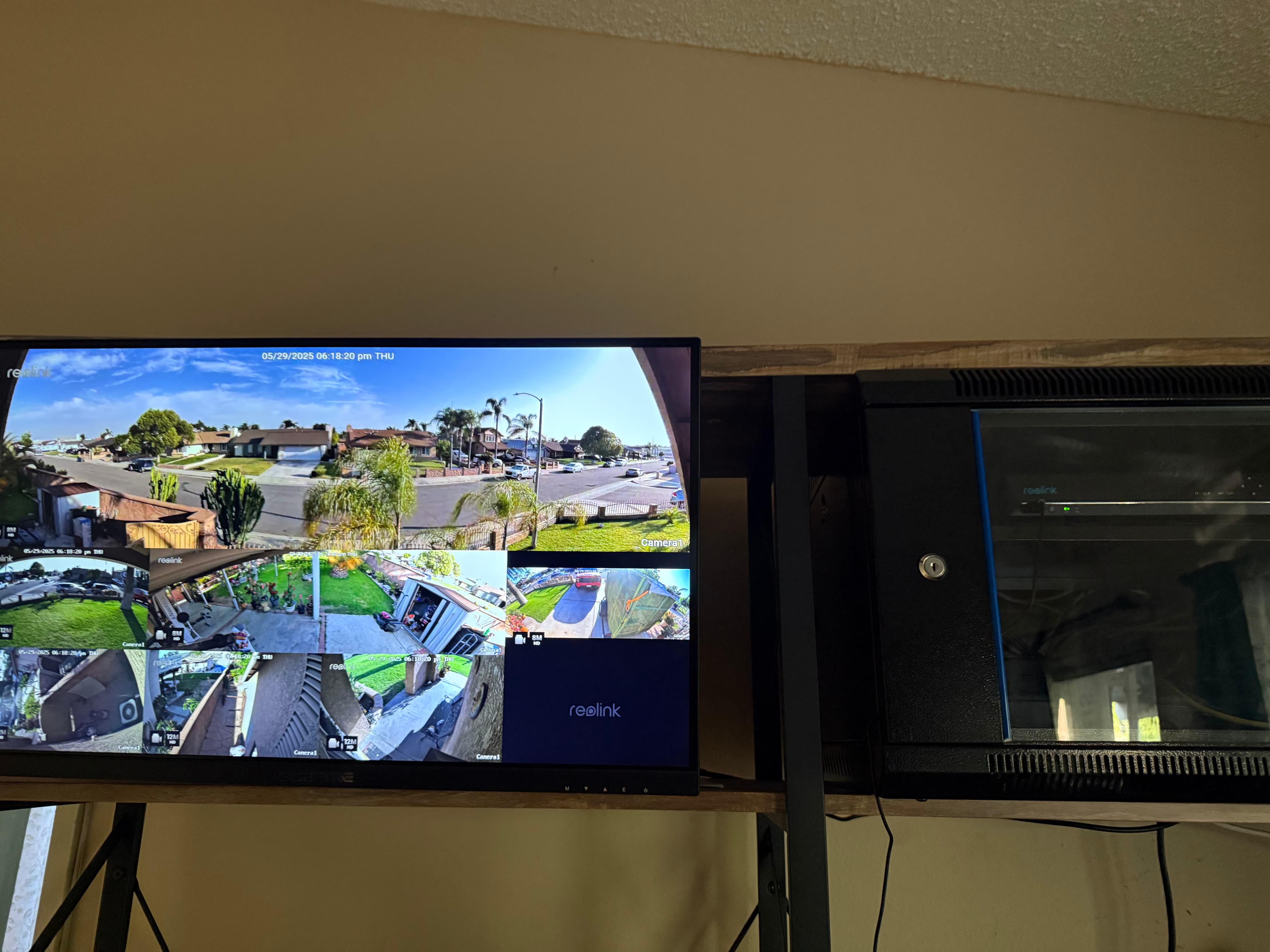 A Reolink security monitor showing multiple outdoor camera feeds next to a black server rack.